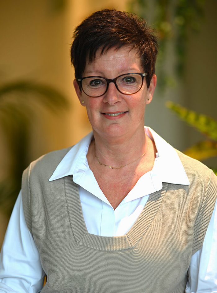 Miriam draagt een witte blouse met een bruine trui