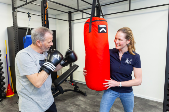 Een fysiotherapeut ondersteunt de boksbal zodat een man kan sporten/boksen voor zijn rugklachten